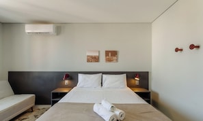 A hotel room with a bed, two bedside tables, a wall-mounted air conditioner, and two wall-mounted lamps. - Comfort w/ Pool Close to Ccmq Tco1215 (Porto Alegre)