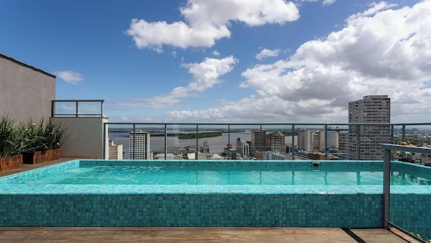 En pool på taket med utsikt över staden, omgiven av byggnader och en klar himmel.