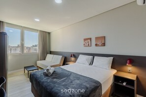 A hotel room with a large bed, a small bedside table, a chair, and a view of the city through large windows. - Studio in Historic Center Near Santa Tco1104 (Porto Alegre)