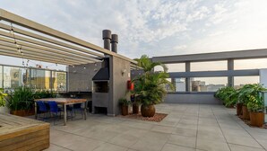 En takterrass med grill, sittplats och planterade blommor och växter i krukor.