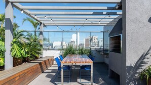 Eine Terrasse im Freien mit einem Holztisch und blauen Stühlen, umgeben von Blumentöpfen.