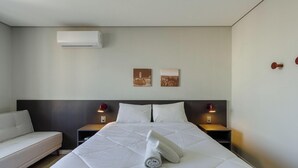 Ein Hotelzimmer mit einem Bett, zwei Nachttischen, einer Wand-Klimaanlage und zwei Wandbildern.