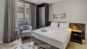 Quarto de hotel moderno com cama, uma cadeira, mesa de cabeceira e janela com cortinas.