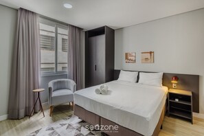 Ein modernes Hotelzimmer mit Bett, Stuhl, Nachttisch und einem Fenster mit Vorhängen.