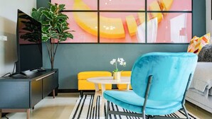 Ein modernes Wohnzimmer mit Fernseher, blauem Sessel, gelber Couch und einem gestreiften Teppich.