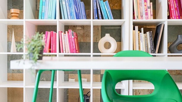 Ein Zimmer mit einem weißen Tisch, einem grünen Stuhl und einem Bücherregal voller Bücher.