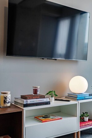 A modern living room with a flat-screen TV mounted on the wall, a white console table with books, a candle, and a potted plant. - Stay Together: 3 Apts, Rooftop & Gym Near Reforma (Mexico City)