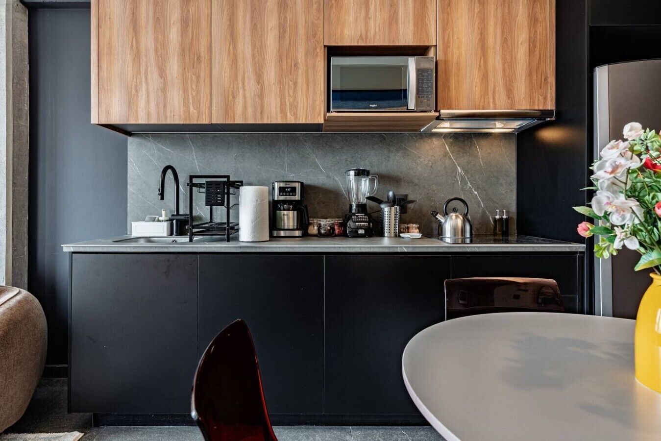 Eine moderne Küche mit Holzschränken, einer Mikrowelle, einer Kaffeemaschine und einem Wasserkocher.