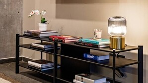 A modern living room with a mounted flat-screen TV displaying a landscape, a black entertainment unit with books and a decorative lamp, and a small potted plant. - Stay Together: 3 Apts, Rooftop & Gym Near Reforma (Mexico City)