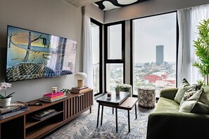 A modern living room with a large window, a flat-screen TV, a green sofa, and a bookshelf with books. - Stay Together: 3 Apts, Rooftop & Gym Near Reforma (Mexico City)