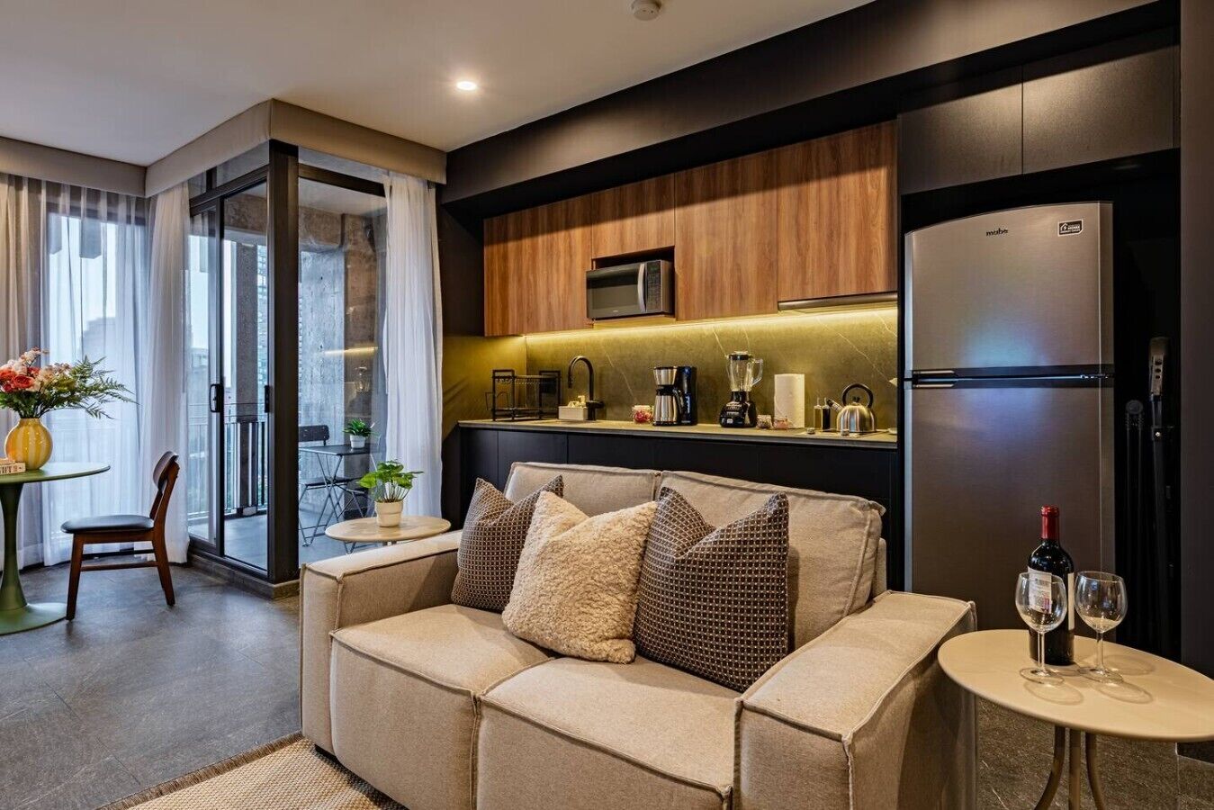 A modern living room with a sofa, a dining area with a table and chairs, and a kitchen area with appliances.