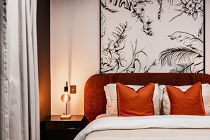 A bedroom with a bed, pillows, a nightstand, a lamp, and a wall with floral artwork. - Stay Together: 3 Apts, Rooftop & Gym Near Reforma (Mexico City)