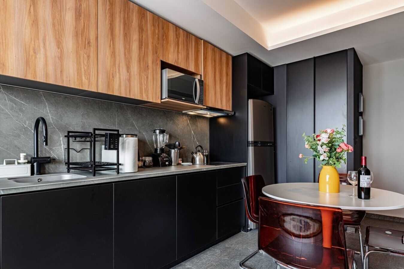 Una cocina moderna con una isla central, armarios negros, un refrigerador de acero inoxidable y un comedor con una mesa redonda y sillas.