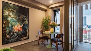 A room with a large classical painting, a dining table with chairs, a vase with flowers, and a view through a window. - Stay Together: 3 Apts, Rooftop & Gym Near Reforma (Mexico City)
