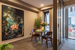 A room with a large classical painting, a dining table with chairs, a vase with flowers, and a view through a window. - Stay Together: 3 Apts, Rooftop & Gym Near Reforma (Mexico City)