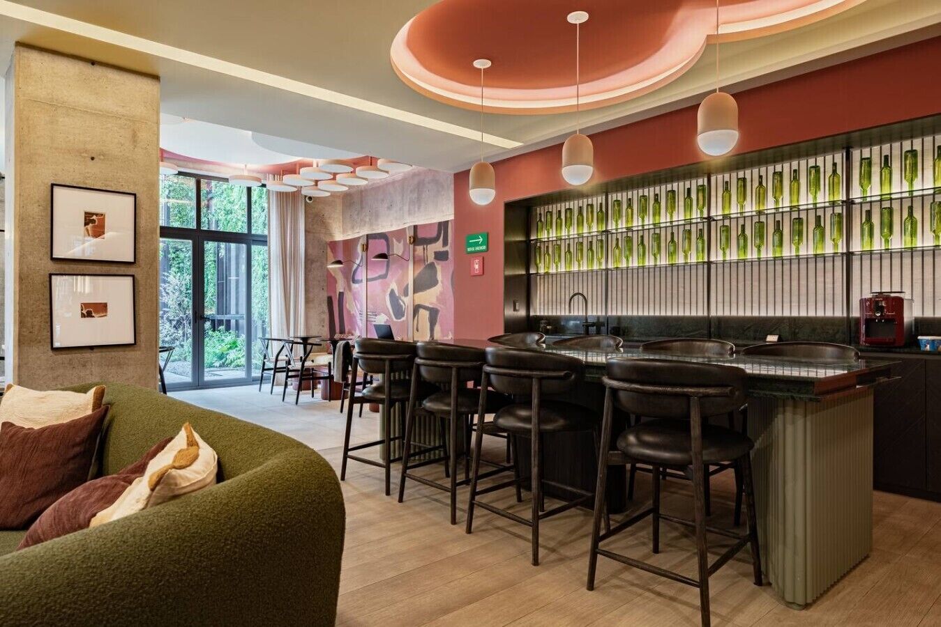 Un área de bar moderna con mostrador, taburetes y una pared de botellas verdes.