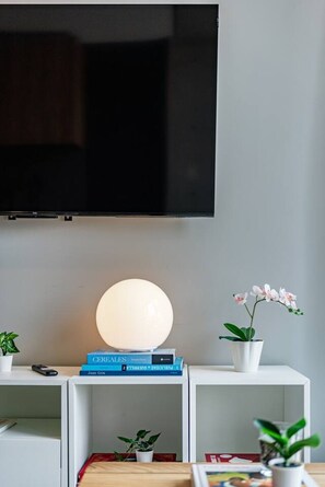 A modern living room with a flat-screen TV mounted on the wall, a round table with a lamp, books, and a potted orchid. - Stay Together: 3 Apts, Rooftop & Gym Near Reforma (Mexico City)