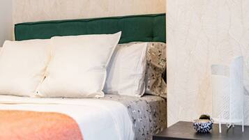 Uma cama bem arrumada com roupa de cama branca e estampada, cabeceira estofada verde e uma mesa de cabeceira com um objeto decorativo.