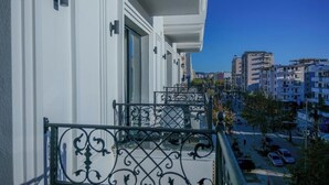 A balcony with wrought iron railings, a white exterior wall, and a clear view of the street below. - Hotel Lubjana (Durrës)