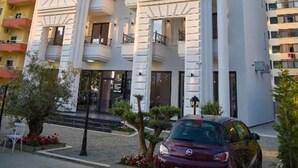 A multi-story hotel with a central entrance, balconies, and a car parked in front. - Hotel Lubjana (Durrës)