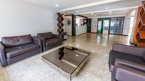 A lobby with leather sofas, a glass coffee table, and a reception area with a counter and glass doors. - Hotel Alvorada Taguatinga (Taguatinga)
