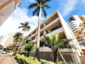 Um edifício de vários andares com varandas, rodeado por palmeiras e um céu limpo.