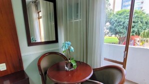 A room with a round wooden table, two chairs, a mirror on the wall, and a view of greenery outside. - Hotel Alvorada Taguatinga (Taguatinga)