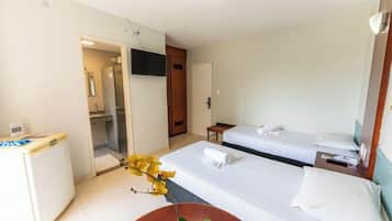 Quarto de hotel com duas camas, uma escrivaninha, televisão e banheiro visível por uma porta aberta.
