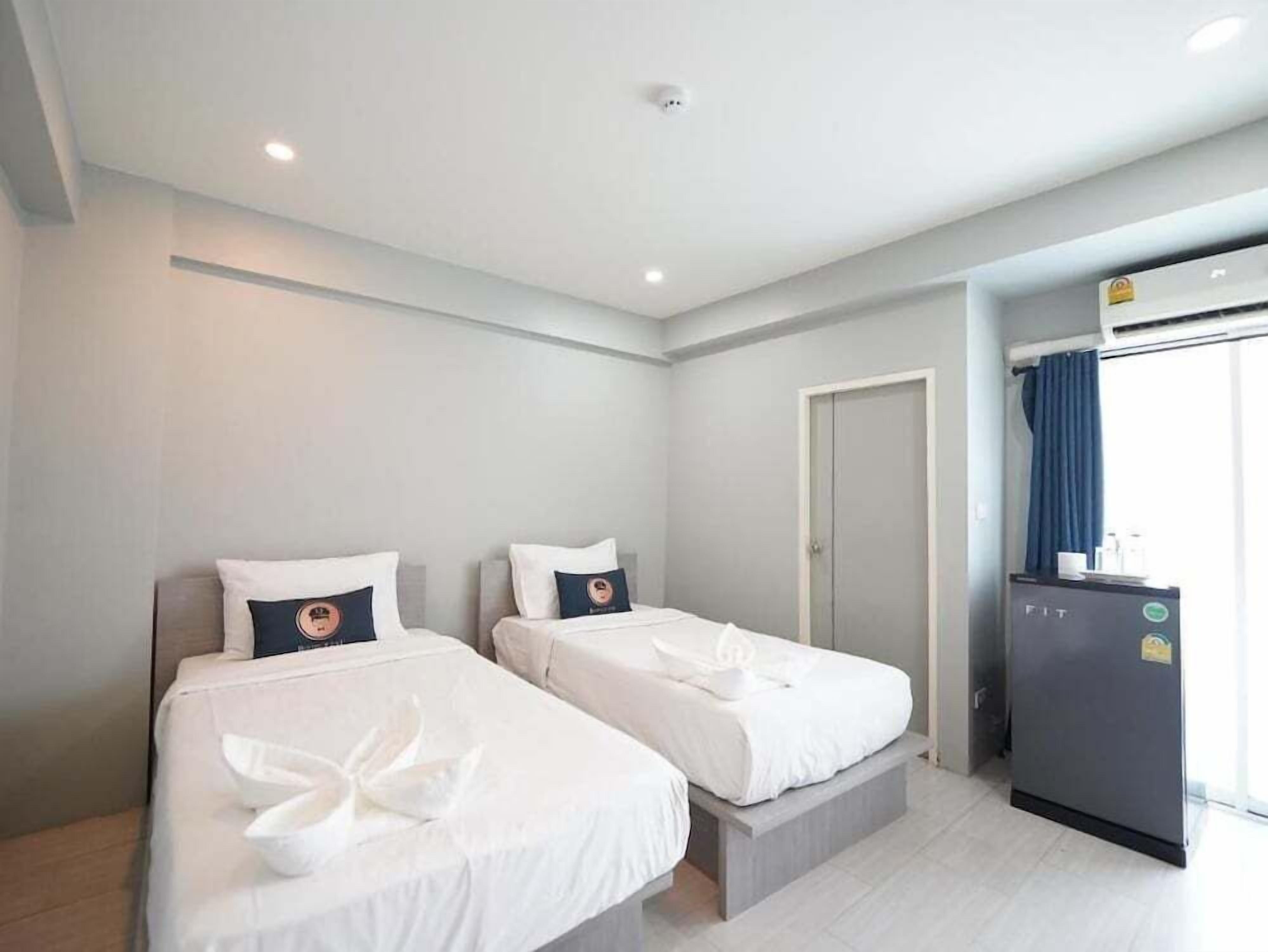 A hotel room with two beds, a small kitchenette, and a door leading to a bathroom.