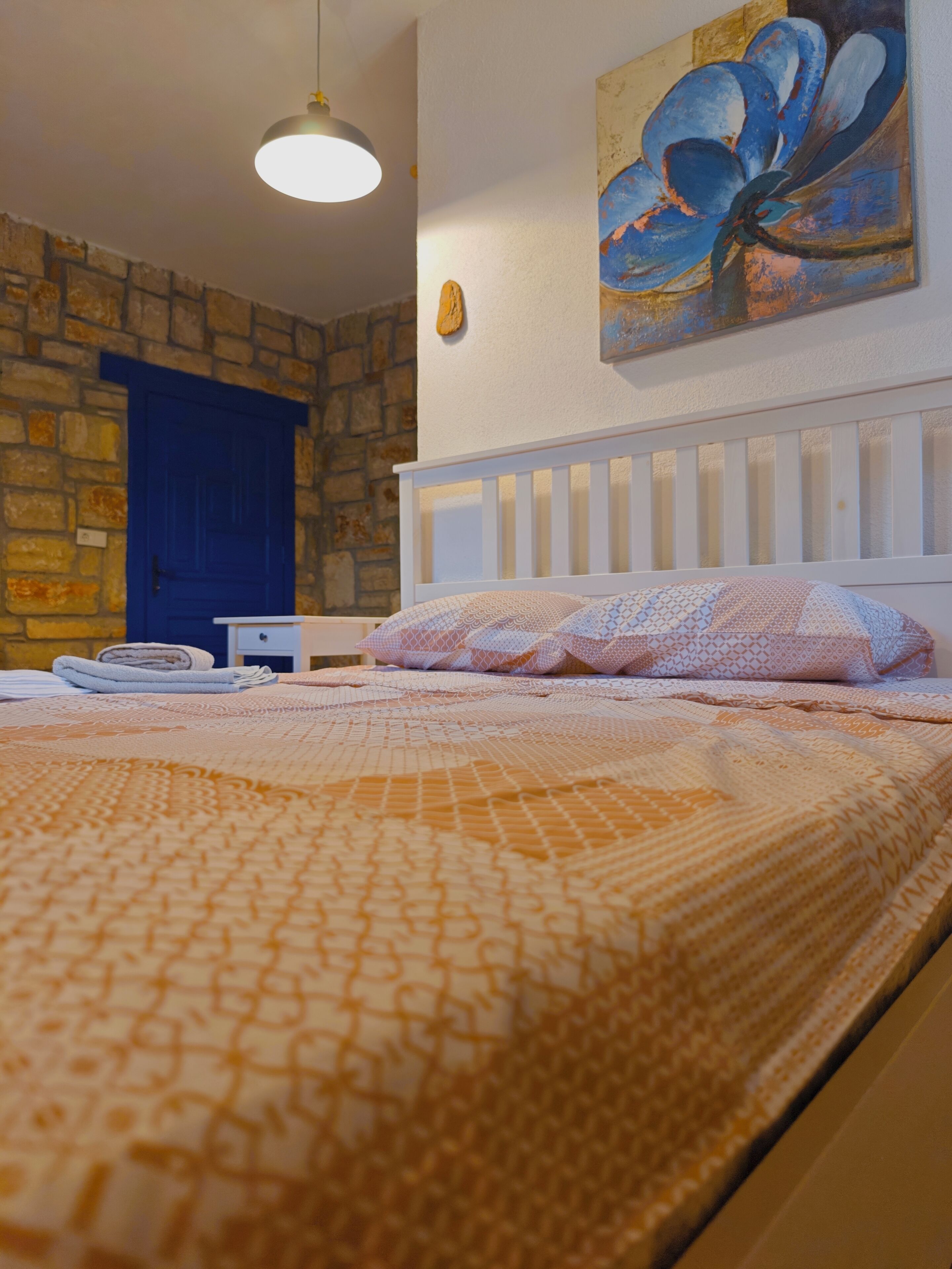 Une chambre à coucher avec un lit, une porte bleue, un tableau et un mur en pierre.
