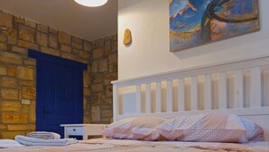 Ein Schlafzimmer mit einem Bett, einer blauen Tür, einem Gemälde und einer Steinwand.