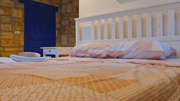 Une chambre à coucher avec un lit, une porte bleue, un tableau et un mur en pierre.