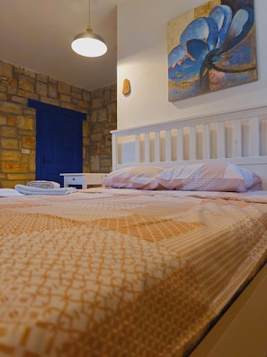 A bedroom with a bed, a blue door, a painting, and a stone wall.