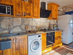 A kitchen with wooden cabinets, a stone wall, a washing machine, a stove, and a refrigerator.