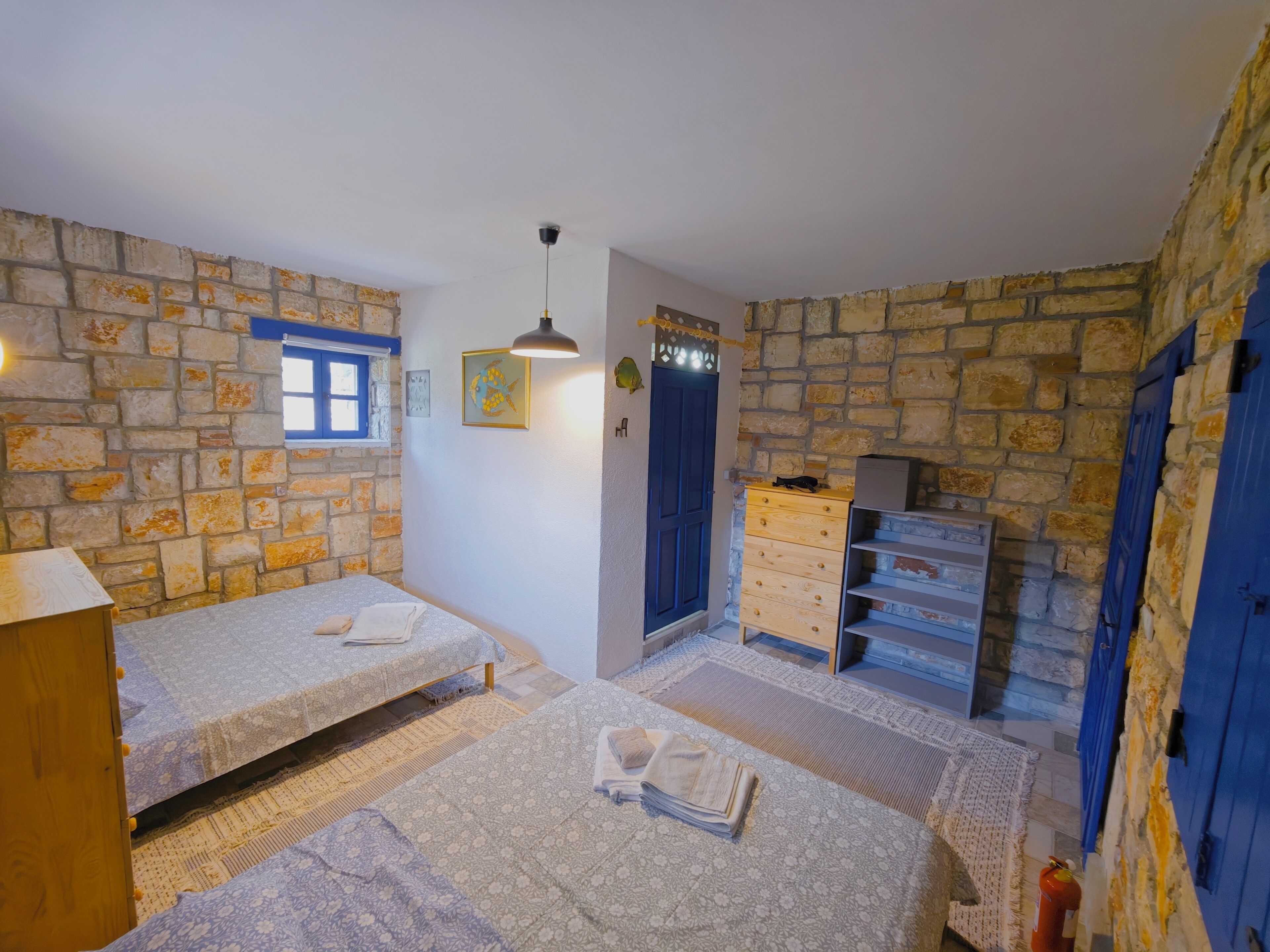 Una habitación con dos camas, un aparador, una ventana y paredes de piedra.
