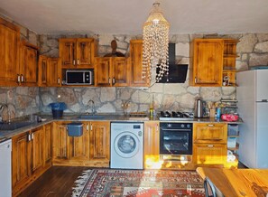 Una cocina con armarios de madera, pared de piedra, lavadora, estufa y una araña.