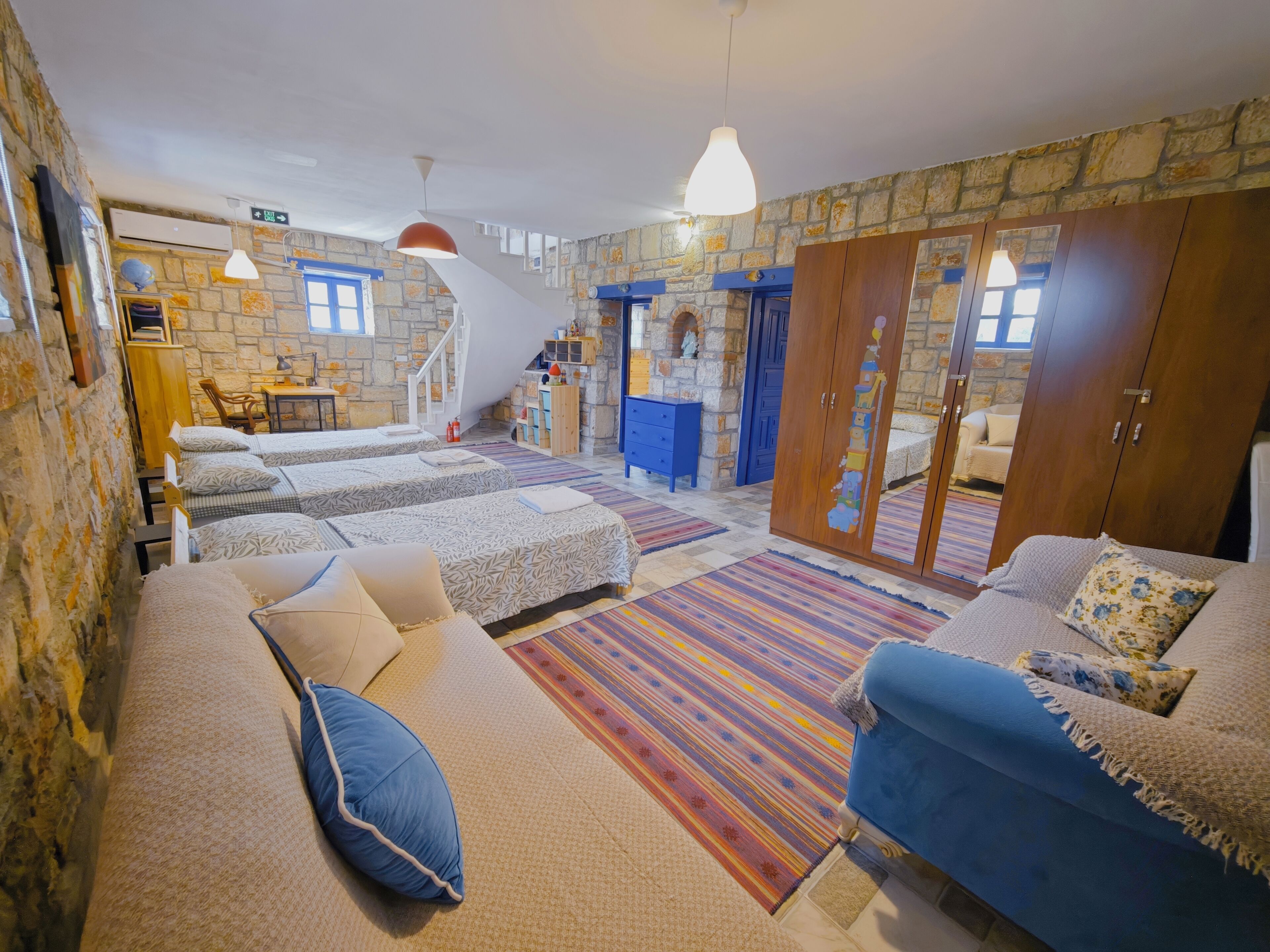 Una habitación con pared de piedra, una escalera, un sofá azul y una cama con ropa de cama estampada.