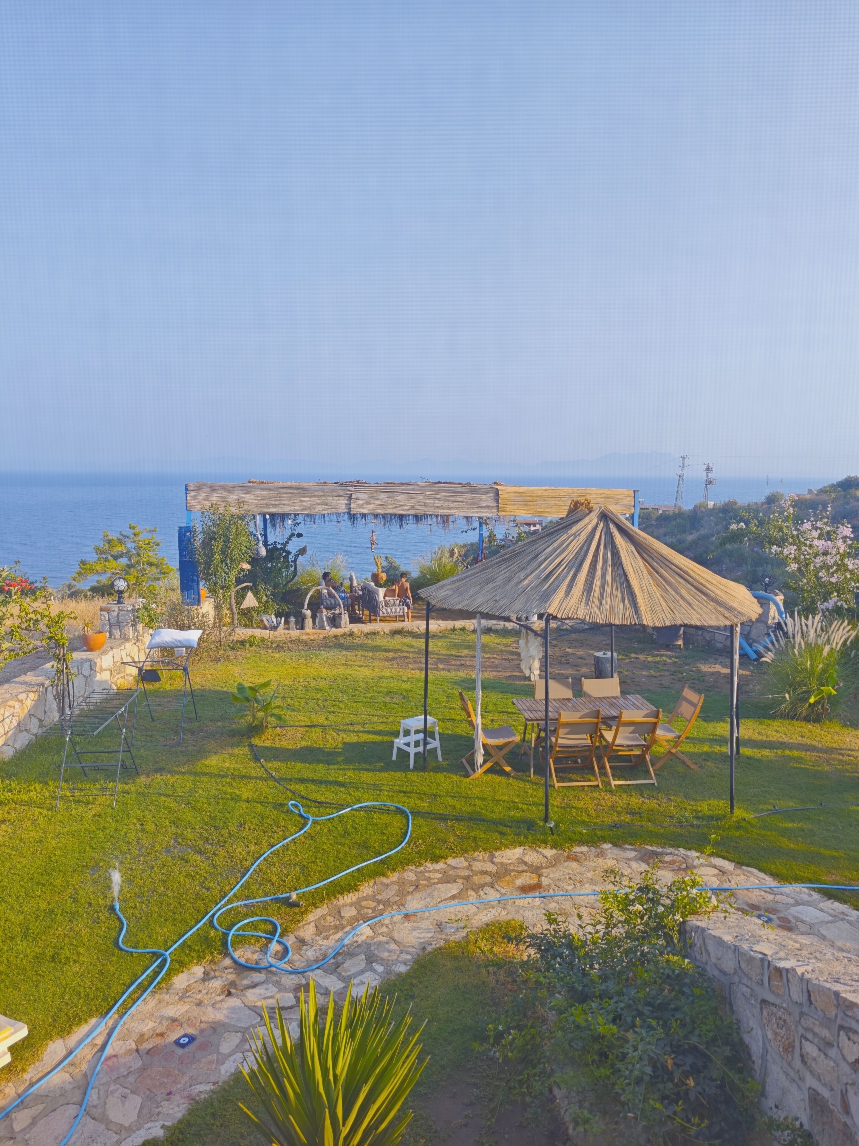 Eine Terrasse mit Tisch und Stühlen, eine strohgedeckte Struktur und Blick auf das Meer.