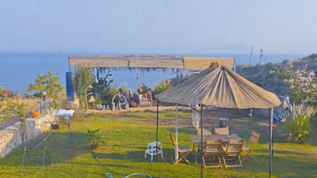 Eine Terrasse mit Tisch und Stühlen, eine strohgedeckte Struktur und Blick auf das Meer.