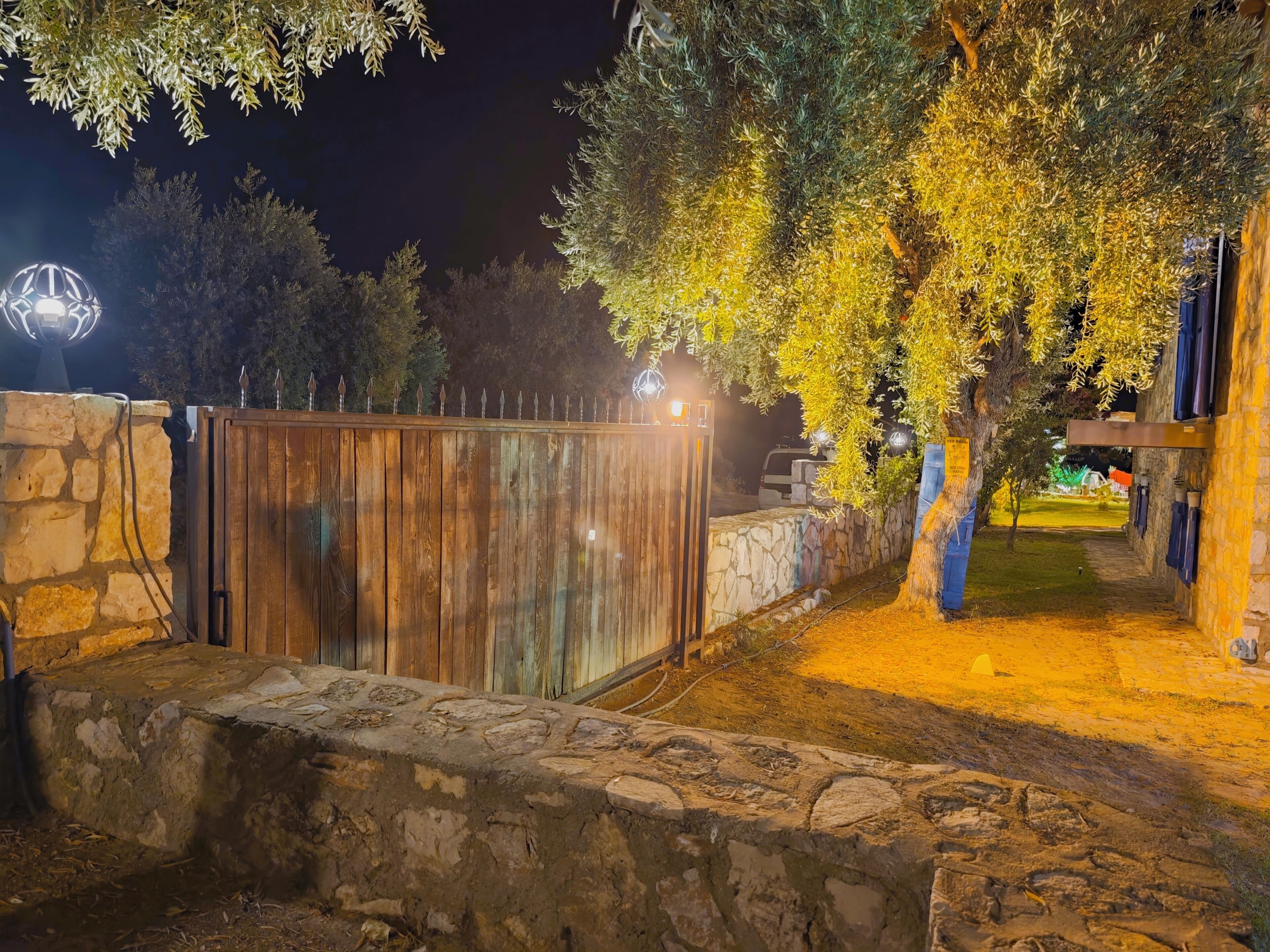 A stone wall, wooden fence, and a tree with yellow leaves at night.