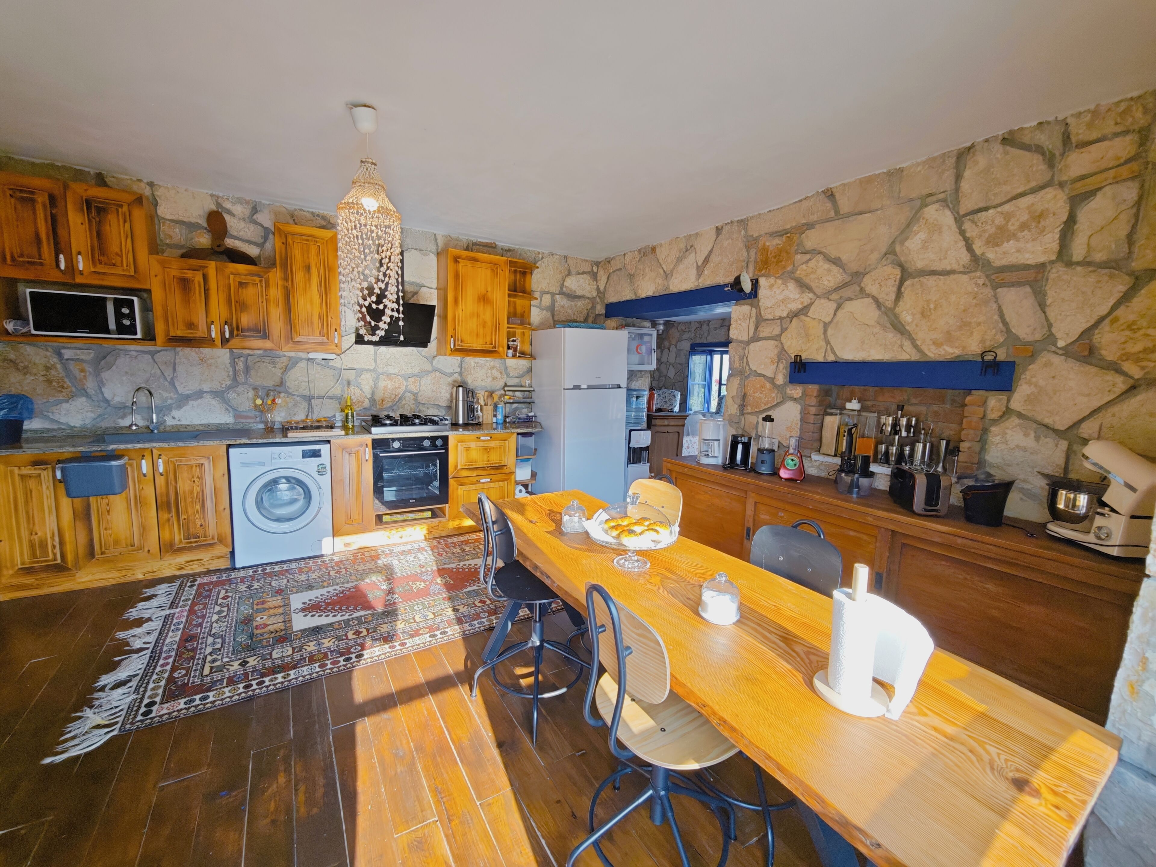 A kitchen with wooden cabinets, a stone wall, a dining table, and various appliances.