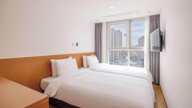 A hotel room with two beds, a TV, and a window with a city view.