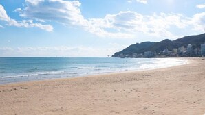 A beach with a clear sky, calm sea, and buildings on a hillside.