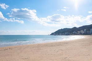 A beach with a clear sky, calm sea, and buildings on a hillside.