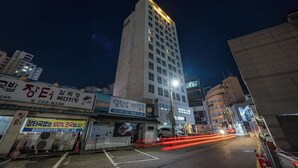 A nighttime urban street with a tall building, illuminated signs, and a parked car.