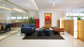 A modern hotel lobby with a seating area, a reception desk, and a glass wall.