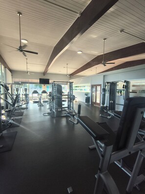 Ein Fitnessraum mit Deckenventilatoren, Trainingsgeräten und großen Fenstern.