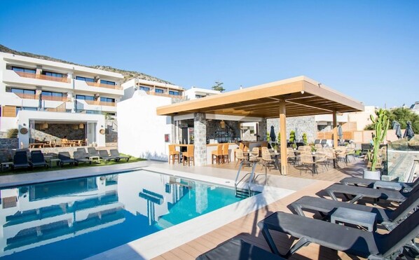 A pool area with lounge chairs, a bar, and a covered seating area.