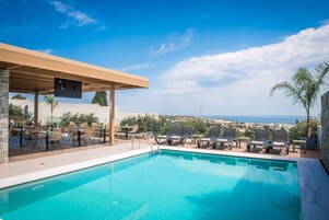 Área de piscina com espreguiçadeiras e um espaço de estar coberto, com vista para uma paisagem deslumbrante.