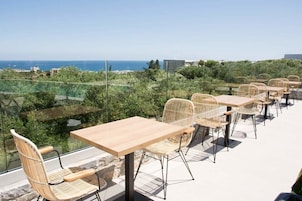 Terraza exterior con mesas y sillas de mimbre, con vistas a un paisaje costero.